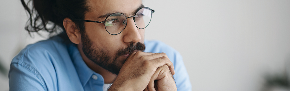 depressed or serious man with beard and round glasses sits thinking