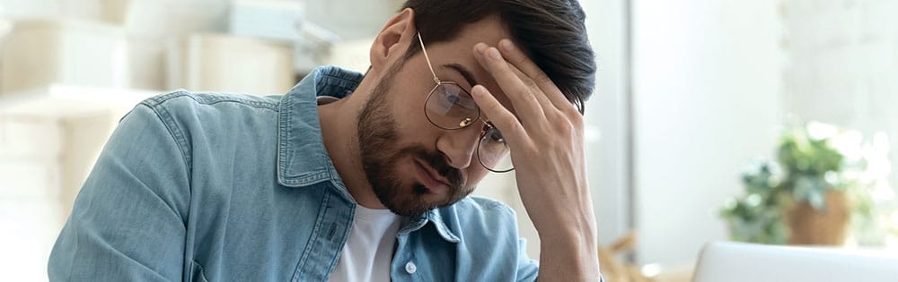 man stressed wears glasses hand on head